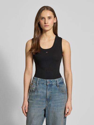 Modelka nosi Slim Fit Tank Top aus Baumwoll-Mix od Tommy Jeans, czarny, logo na piersi, krój slim fit, dzianina prążkowana, pełny przód, ujęcie całej sylwetki z przodu.