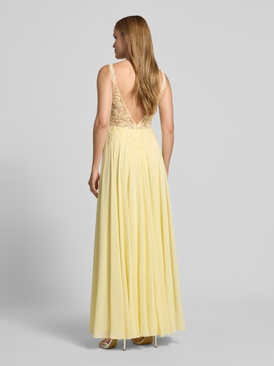 Frauenmodel trägt Abendkleid mit floralem Spitzenbesatz von Mascara in Gelb, semitransparent, Tailliert, Paillettenbesatz, Ärmelloses-Design, V-Ausschnitt, Rückenlänge 135 cm, Brustweite 32 cm, Ganzkörperansicht Rückansicht.