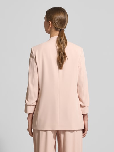 Frauenmodel trägt Blazer mit Pattentaschen von Jake*s Collection im zarten Rosaton, Material-Mix mit Stretch-Anteil, lockerer Schnitt, Stehkragen, 3/4-Ärmel, Rückenlänge 69 cm, Brustweite 44 cm, Ärmel 52 cm, Ganzkörperansicht Rückansicht.