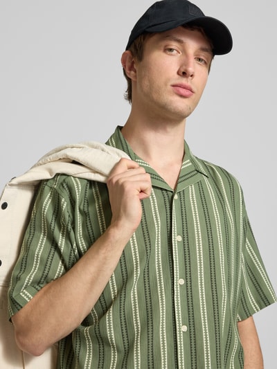 Männermodel trägt Regular Fit Freizeithemd mit Reverskragen Modell 'HOWIE' von Redefined Rebel, Allover-Look grün gestreift, Reine Baumwolle, Label-Detail, Nahaufnahme Oberkörper.
