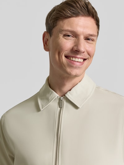 Mężczyzna nosi Blouson mit Kentkragen von JAKE*S STUDIO MEN, jasny kolor, krój regular fit, zamek, kentkragen, zbliżenie na górę ciała. Szerokość w rozmiarze M: 58 cm, długość tyłu: 60 cm, długość rękawa: 67 cm, szerokość ramion: 48 cm.
