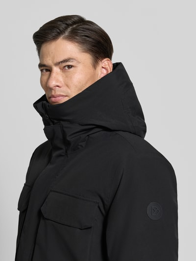 Männermodel trägt Parka mit Kapuze und Pattentaschen Modell 'AIDEN' von Didriksons in Schwarz, Nahaufnahme Oberkörper, Regular Fit, verdeckter Reißverschluss, KI-modifiziertes Bild.