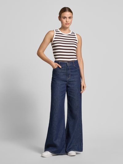 Frauenmodel trägt Slim Fit Top mit Rundhalsausschnitt Modell 'Effy' von FREE/QUENT in Weiß und Dunkelbraun, elastischer Baumwoll-Mix, gestreiftes Muster, kombiniert mit blauer Wide-Leg-Jeans, Ganzkörperansicht von vorne.