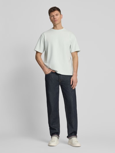 Męski model nosi Oversized T-Shirt mit Rundhalsausschnitt von Lindbergh z bawełny, detal z logo, kolor jasny, długość tyłu w rozmiarze M: 70 cm, krój oversized, okrągły dekolt, ganzkörperansicht von vorne.