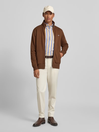 Männermodel trägt Sweatjacke mit Label-Stitching von Gant, braun, Baumwoll-Mix, Regular-Fit, Stehkragen, Reißverschluss, Ganzkörperansicht von vorne.