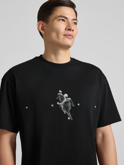 Männermodel trägt Regular Fit T-Shirt aus reiner Baumwolle Modell 'DOLLO' von HUGO, schwarz, grafisch gemustert, Rundhals, Nahaufnahme Oberkörper.