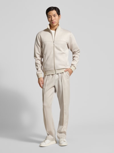 Męski model nosi Track Pants mit Eingrifftaschen Modell 'Ballier' od Les Deux, beżowy materiał z elastycznym pasem i francuskimi kieszeniami, materiał-mix ze stretchem, prosty krój, widok całej sylwetki z przodu.