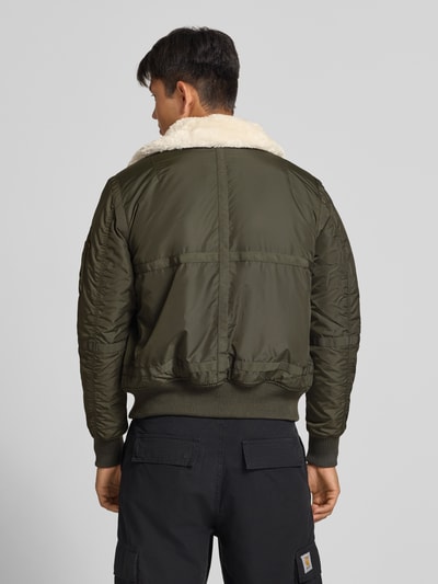 Männermodel trägt Bomberjacke mit Label-Patch und Kentkragen von Alpha Industries in Olivgrün, Teddyfellkragen, Rückansicht, Ganzkörperansicht Rückansicht. Regular Fit, Reißverschluss, gerippte Abschlüsse, Reißverschlusstasche am Ärmel, Eingrifftaschen mit Druckknopfverschluss, Rückenlänge 65 cm, Schulterbreite 45 cm, Brustweite 56 cm, Ärmellänge 65 cm.