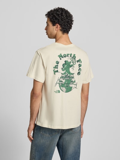 Mężczyznamodel nosi Relaxed Fit T-Shirt mit Logo-Print von The North Face z bawełny, okrągły dekolt, krój relaxed fit, długość tyłu 70 cm w rozmiarze M, kolor ecru z zielonym nadrukiem z logo, całkowity widok z tyłu.