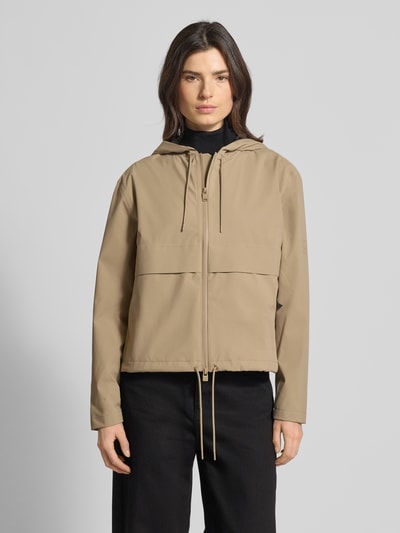 Frauenmodel trägt Regular Fit Jacke mit Kapuze Modell 'Suva' von Rains in Beige mit Zweiwege-Reißverschluss, Tunnelzug im Bund, Ganzkörperansicht von vorne. Rückenlänge 59 cm, Schulterbreite 49 cm, Brustweite 54 cm, Ärmellänge 60 cm bei Größe S.