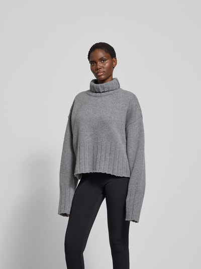 Frauenmodel trägt Oversized Pullover aus reiner Wolle von black palms in Grau mit gerippten Abschlüssen und Rollkragen, Ganzkörperansicht von vorne. Rückenlänge bei Größe S: 56 cm.