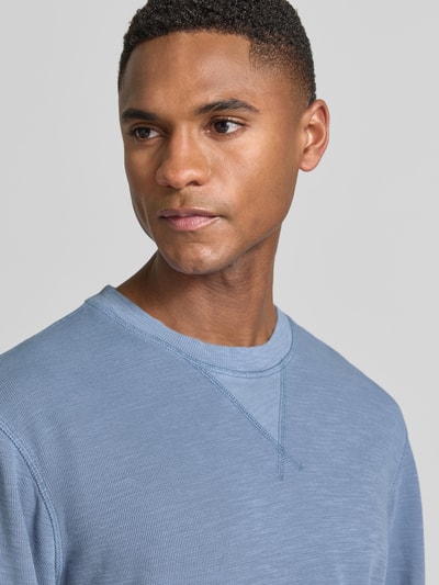 Männermodel trägt Regular Fit Sweatshirt mit Rundhalsausschnitt von Scotch & Soda aus Baumwoll-Mix in Hellblau, Label-Detail, Nahaufnahme Oberkörper. Rückenlänge bei Größe M: 68 cm, Ärmellänge: 65 cm.