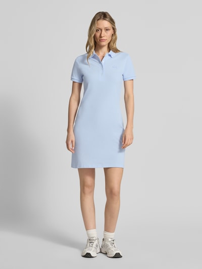 Frauenmodel trägt Slim Fit Polokleid aus Baumwoll-Mix von Lacoste in Hellblau mit kurzem Arm, Logo-Stitching, Piqué-Struktur, Ganzkörperansicht von vorne.