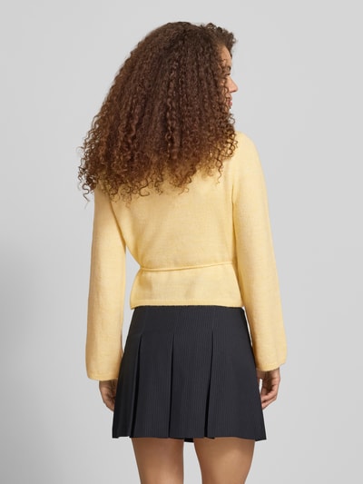 Frauenmodel trägt Regular Fit Strickjacke mit Woll-Anteil Modell 'COLO' von Only in Melange-Optik, Wickeloptik, Stricktextur, Ganzkörperansicht Rückansicht.