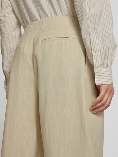 Männermodel trägt Stoffhose aus Viskose-Leinen-Mix von MAISON KITSUNÉ in Beige mit Kellerfalten, Nahaufnahme Rückansicht