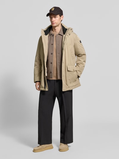 Männermodel trägt Parka mit Kapuze und Pattentaschen von MCNEAL in Beige, Regular Fit, verdeckter Reißverschluss, Ganzkörperansicht von vorne. Rückenlänge 85 cm, Schulterbreite 49 cm, Brustweite 46 cm, Ärmellänge 67 cm.