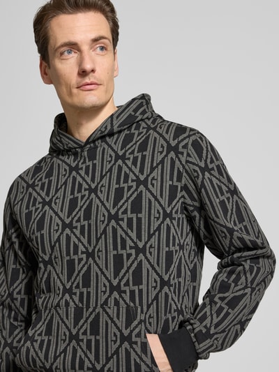 Männermodel trägt Hoodie im Allover-Look mit Känguru-Tasche von Guess aus reiner Baumwolle, Regular-Fit, Nahaufnahme Oberkörper.