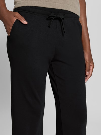 Frauenmodel trägt Flared Fit Sweatpants mit Tunnelzug von Juvia, schwarze Farbe, elastischer Baumwoll-Modal-Mix, Nahaufnahme Oberkörper.