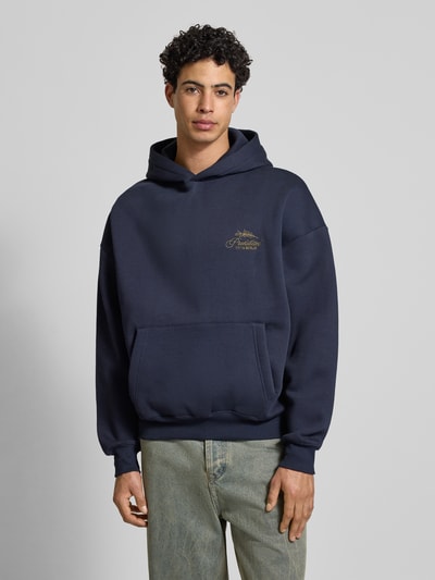 Männermodel trägt Oversized Hoodie mit Label-Stitching von PROHIBITED in Dunkelblau, Baumwoll-Mix, Känguru-Tasche, gerippte Abschlüsse, Ganzkörperansicht von vorne. Rückenlänge 67 cm, Ärmellänge 59 cm, Größe M.