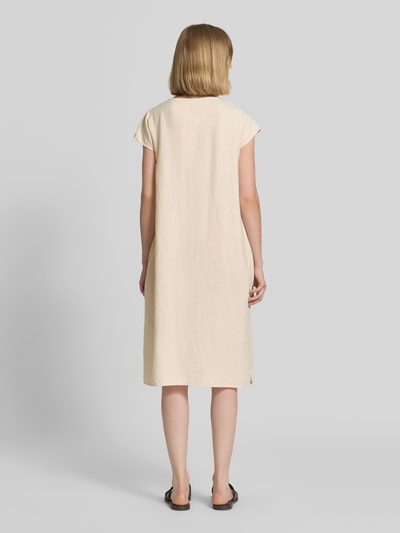 Vrouwenmodel draagt Knielanges Leinenkleid mit V-Ausschnitt Modell 'Ina' van Soyaconcept, linnenmix met viscose, loose fit, knielengte, zijsplitten, ruglengte maat S 105 cm, borstwijdte 51 cm, mouwlengte 7 cm, effen licht beige, rechte vormen, zachte textuur. Ganzkörperansicht Rückansicht.