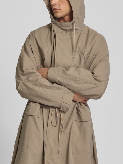 Męski model nosi Parka mit Pattentaschen od MAISON KITSUNÉ w kolorze beżowym, tekstura żakardowa, luźny krój, przód z patkami i kapturem, zamek błyskawiczny z plisą, kieszenie z patką, tunel w talii, Długość tyłu w rozmiarze M: 122 cm, Szerokość ramion w rozmiarze M: 43 cm, Długość rękawów w rozmiarze M: 69 cm, Ganzkörperansicht z przodu
