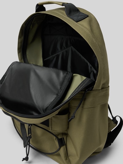 Produktfoto, Rucksack mit Label-Detail Modell 'KICKFLIP' von Carhartt Work In Progress in Oliv mit Hauptfach, Reißverschluss, Tragehenkel, gepolsterten verstellbaren Schulterriemen, 34 cm Breite, 45 cm Länge, 20 cm Tiefe, 70 cm Länge Schulterriemen, glatte und matte Textur, schwarz abgesetztes Innenfutter.