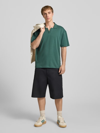 Męski model nosi Boxy Fit Poloshirt aus Baumwoll-Mix Modell 'CASPIAN AIRLEX' od Only & Sons, zielony, jednokolorowy, krótki rękaw, bawełniany jersey, label patch, polokrag, Ganzkörperansicht von vorne.
