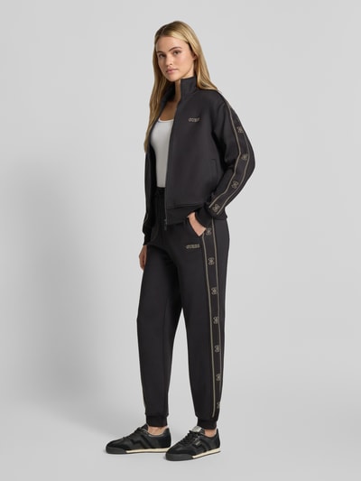 Frauenmodel trägt schwarze Sweatpants mit Label-Detail Modell 'OCTAVIA' von GUESS, regular Fit, elastischer Bund, Ganzkörperansicht von vorne.