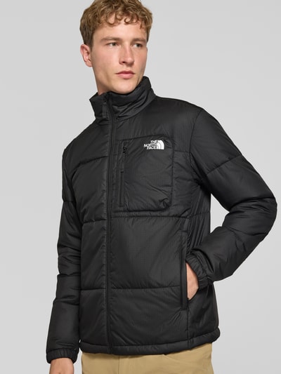 Männermodel trägt schwarze Regular Fit Jacke in Stepp-Optik Modell 'NUKETO' von The North Face mit Stehkragen und Logo-Print, Ganzkörperansicht von vorne. Rückenlänge, Schulterbreite, Brustweite und Ärmellänge gemäß Kontext