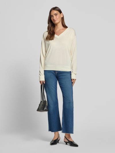 Frauenmodel trägt Regular Fit Pullover aus reiner Schurwolle von BOSS in Creme, kombiniert mit blauer Jeans, Damen Ganzkörperansicht von vorne.