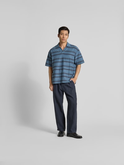 Männermodel trägt Oversized Poloshirt mit Logo-Patch von MAISON KITSUNÉ aus reiner Baumwolle, Oversized-Fit, kurzärmelig, Ganzkörperansicht von vorne.