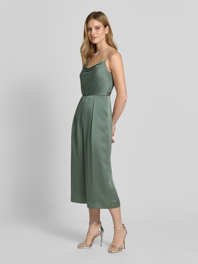 Modelka nosi Jumpsuit aus Satin mit Wasserfall-Ausschnitt von Jake*s Cocktail, satynowy materiał, kolor zielony, krój skrócony, spiczaste nogawki, szerokość w rozmiarze 36: 28 cm, długość całkowita: 114 cm, długość wewnętrzna nogawki: 56 cm, widok całej sylwetki z przodu.