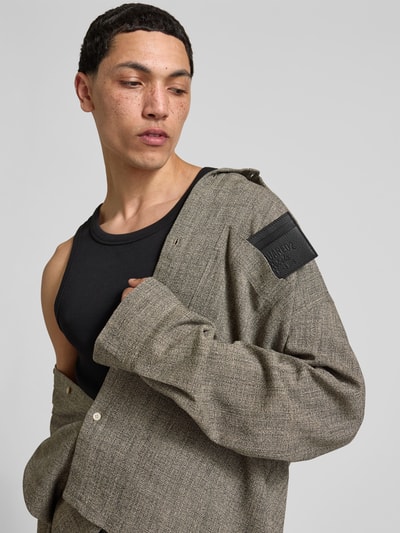 Männermodel trägt schwarze Jacke mit Logo-Prägung von Dsquared2, graues Strukturmuster, Nahaufnahme Oberkörper.