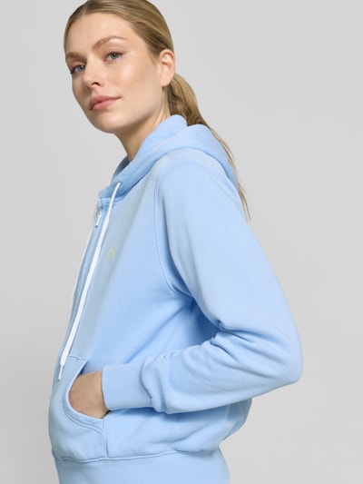 Frauenmodel trägt Regular Fit Sweatjacke aus Baumwoll-Mix von Polo Ralph Lauren in hellblau mit Kapuze, Reißverschluss und Logo-Stitching, Nahaufnahme Oberkörper.