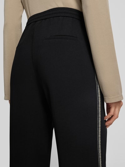 Frauenmodel trägt Hose mit elastischem Bund und Galonstreifen von Marc Cain in Schwarz mit Bügelfalten, Detailaufnahme Rückansicht.