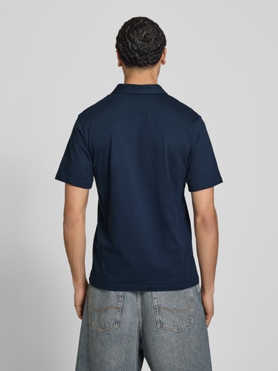 Männermodel trägt poloshirt met labelprint model 'BRANDON' van Jack & Jones, puur katoen, regular fit, polokraag, korte knoopsluiting, ruglengte bij maat M 71 cm, donkerblauw, textuur glad, rechte zoom, ganzlichaamsaanzicht achteraan.