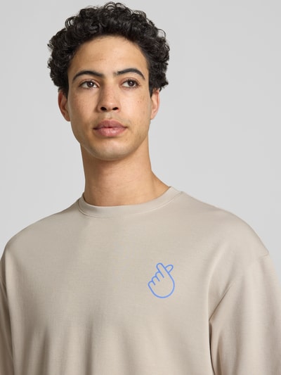 Männermodel trägt Regular Fit T-Shirt aus reiner Baumwolle Modell 'CASPIAN AIRFLEX AMORE' von Only & Sons, unifarben, Rundhals, kurzarm, feuchtigkeitsregulierend und atmungsaktiv, heller Farbton mit kleinem Schriftzug-Print, Nahaufnahme Oberkörper.