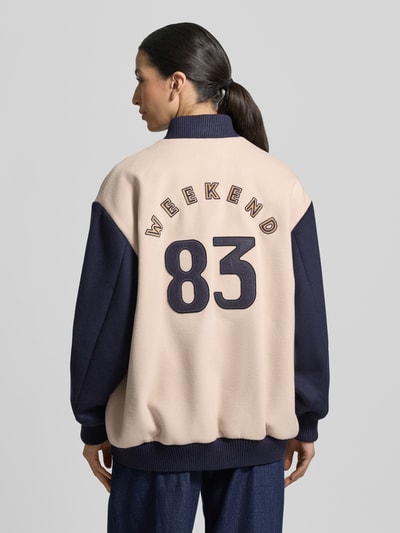 Vrouwenmodel draagt Relaxed fit college-jack uit scheerwolmix model 'ELLISSE' van Weekend Max Mara, effen tweekleurige look, comfort fit, collegekraag, drukknoopsluiting, labelstitching, lange mouwen met geribde mouwboord, geribde rompzoom, zijsteekzakken, detailopname rugaanzicht.