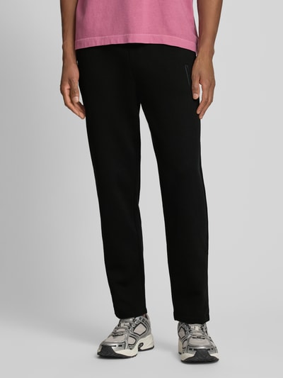 Männermodel trägt zwarte Sweatpants met elastische band en logo van GAP, katoenmix, regular fit, binnenbeenlengte maat M 74 cm, detailaufnahme onderlichaam.
