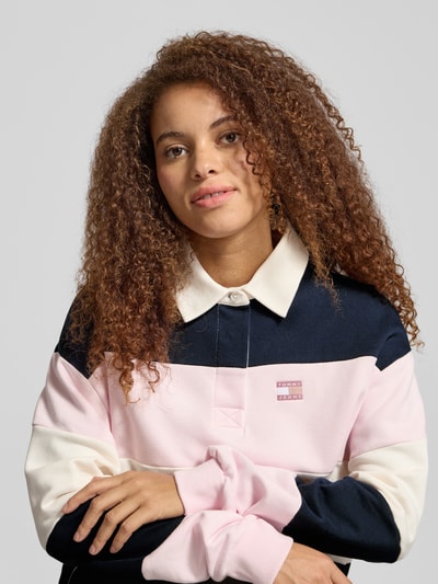 Frauenmodel trägt Regular Fit Pullover aus reiner Baumwolle von Tommy Jeans in mehrfarbiger Optik mit Label-Stitching-Applikation, Polokragen, Langarm, geripptem Ärmelabschluss und Rumpfabschluss, Sweat-Material, Nahaufnahme Oberkörper.