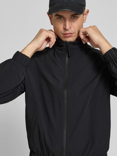 Männermodel trägt Blouson mit Stretch-Anteil von Forét in Schwarz, lockere Passform, Zweiwege-Reißverschluss, Nahaufnahme Oberkörper.