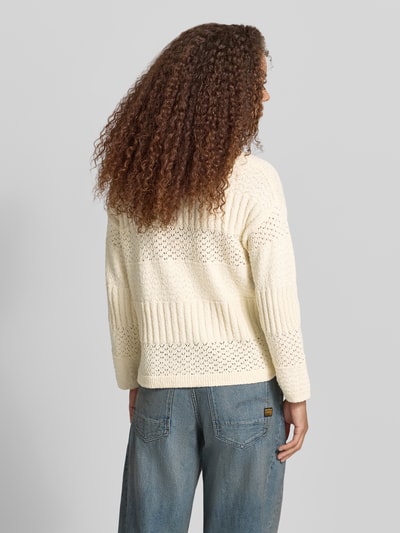 Frauenmodel trägt Boxy Fit Strickpullover aus reiner Baumwolle Modell 'ALAYA' von Pepe Jeans, Strickoptik, Struktur, Rundhals, Langarm, Seitenschlitze, asymmetrisch, Ganzkörperansicht Rückansicht.