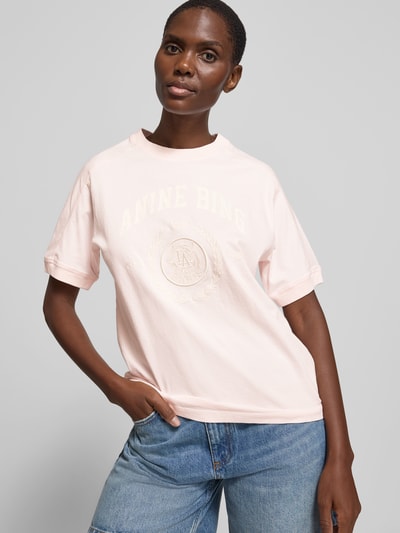 Frauenmodel trägt Regular Fit T-Shirt mit Logo-Print von Anine Bing aus reiner Baumwolle, Rundhalsausschnitt, kurzärmelig, hellrosafarben, Ganzkörperansicht von vorne.