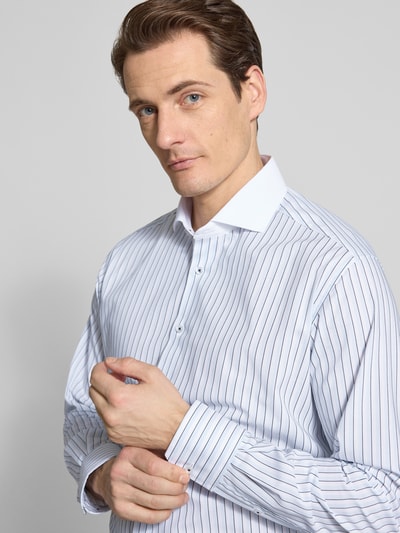 Männermodel trägt Regular Fit Business-Hemd mit Kentkragen von ETERNA aus reiner bawełna, krój regular fit, listwa guzikowa, z długim rękawem, sportowe mankiety, długość tyłu w rozmiarze 40: 79 cm, szerokość ramion w rozmiarze 40: 48 cm, długość rękawów w rozmiarze 40: 64 cm, wzór w paski, kolor biały z granatowymi liniami, nahaufnahme górnej części ciała.