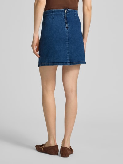 Frauenmodel trägt eng anliegenden Jeansrock aus Baumwoll-Mix Modell 'NELLY' von Vero Moda, Denim-Optik, Mini-Länge, Ganzkörperansicht Rückansicht.