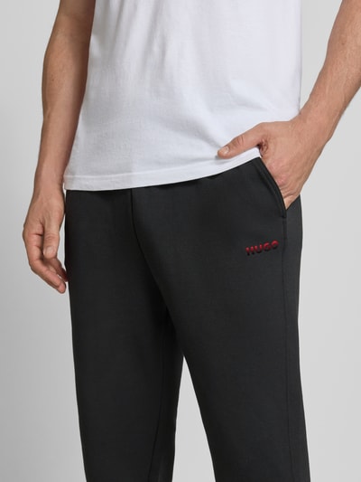 Männermodel draagt Relaxed Fit Sweathose uit katoenmix Model 'ATLAS' van HUGO in effen kleur met labelprint, zij-steekzakken, elastische boord en pijpboord, sweatmateriaal; detailopname van de heup en hand in zak.
