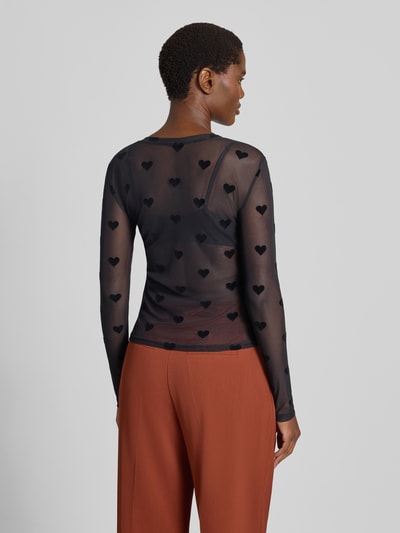 Frauenmodel trägt Slim Fit Langarmshirt mit Rundhalsausschnitt Modell 'LOVA' von VERO MODA, schwarz mit Herzmuster, transparente Optik, Ganzkörperansicht Rückansicht.