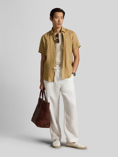 Mannenmodel draagt Regular Fit Leinenhemd mit Button-Down-Kragen van Polo Ralph Lauren in effen beige, van puur linnen, korte mouwen, afgeronde zoom, logo-stitching, volledige knopenlijst, gecombineerd met witte broek, kleuren lichtbruin en wit, voorkant volledig zichtbaar, full-body aanzicht.