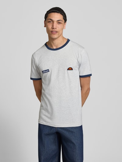 Męski model nosi T-Shirt mit Logo- und Label-Patch Modell 'RINGETTO' od Ellesse, bawełna, krój regular fit, kolor jasnoszary, przód, zdjęcie całej sylwetki.