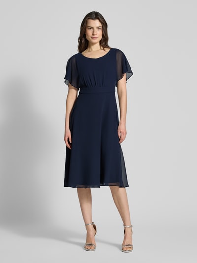 Frauenmodel trägt Knielanges Kleid mit Rundhalsausschnitt von Vera Mont in Dunkelblau, semitransparentes Design, taillierte Passform, Kurzarm, blickdichter Unterrock, Nahtreißverschluss. Ganzkörperansicht von vorne.